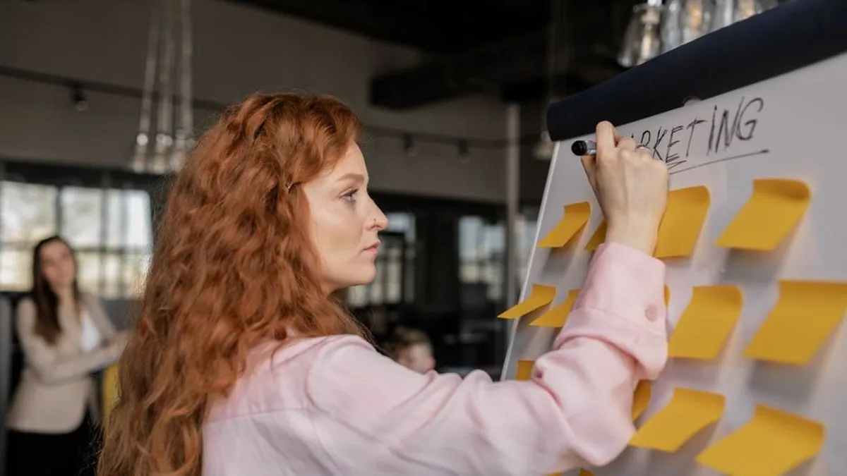 Marketer writing the word marketing on a whiteboard covered in sticky notes