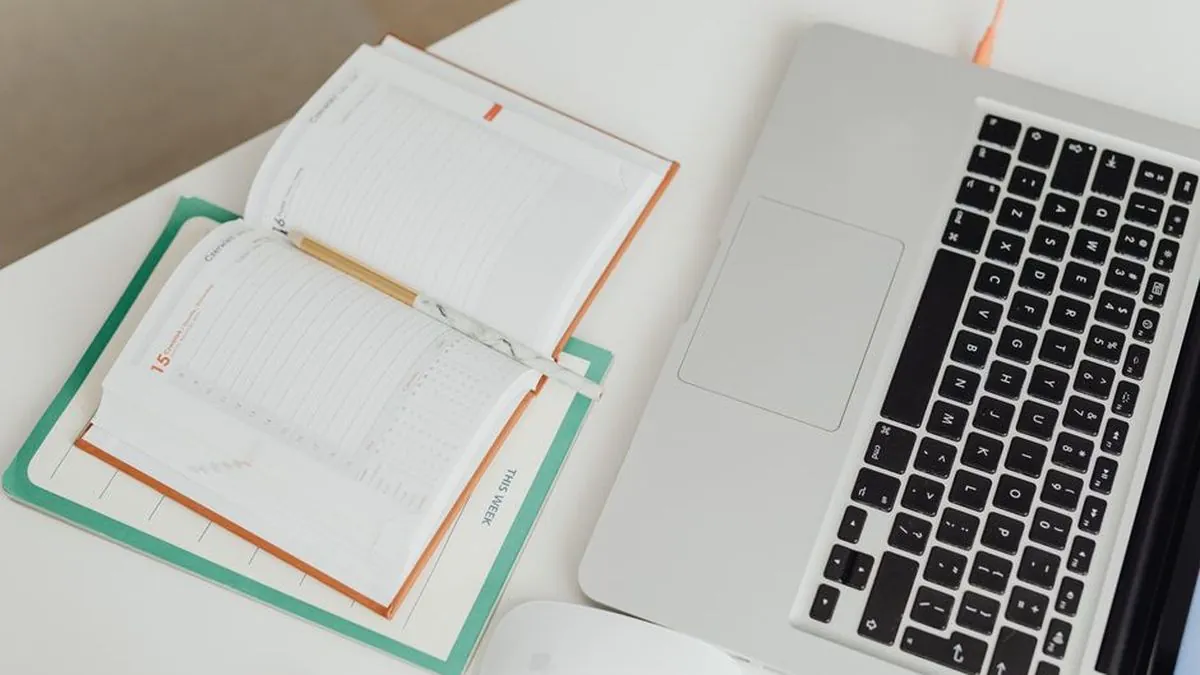 Open planner beside a laptop on a white desk for planning a content calendar
