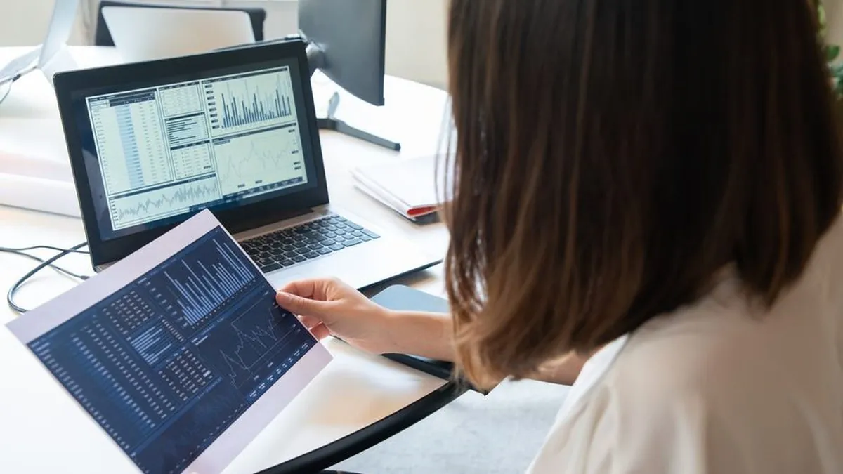 Marketer holding a printed analytics report while a laptop shows website charts