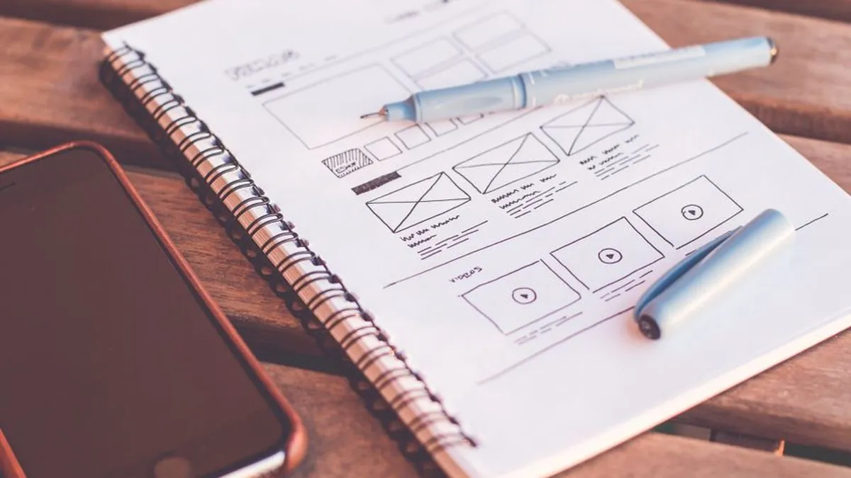 Website wireframe sketched in a spiral notebook beside a smartphone