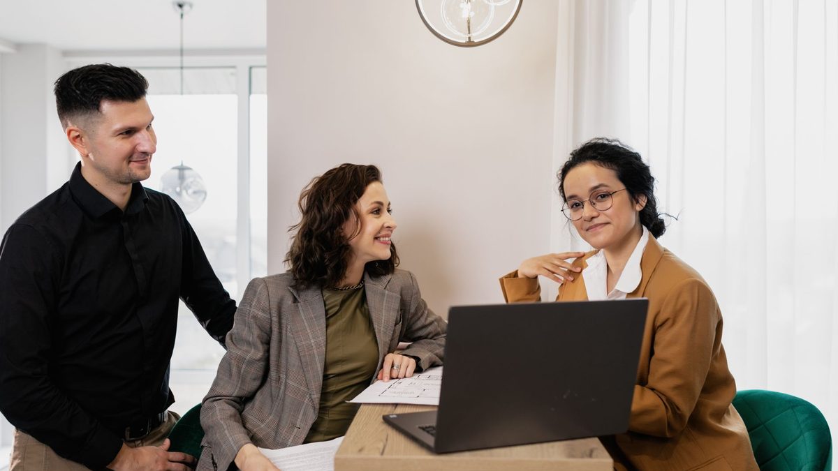 Marketing consultant meeting two clients around a laptop to discuss an ad budget