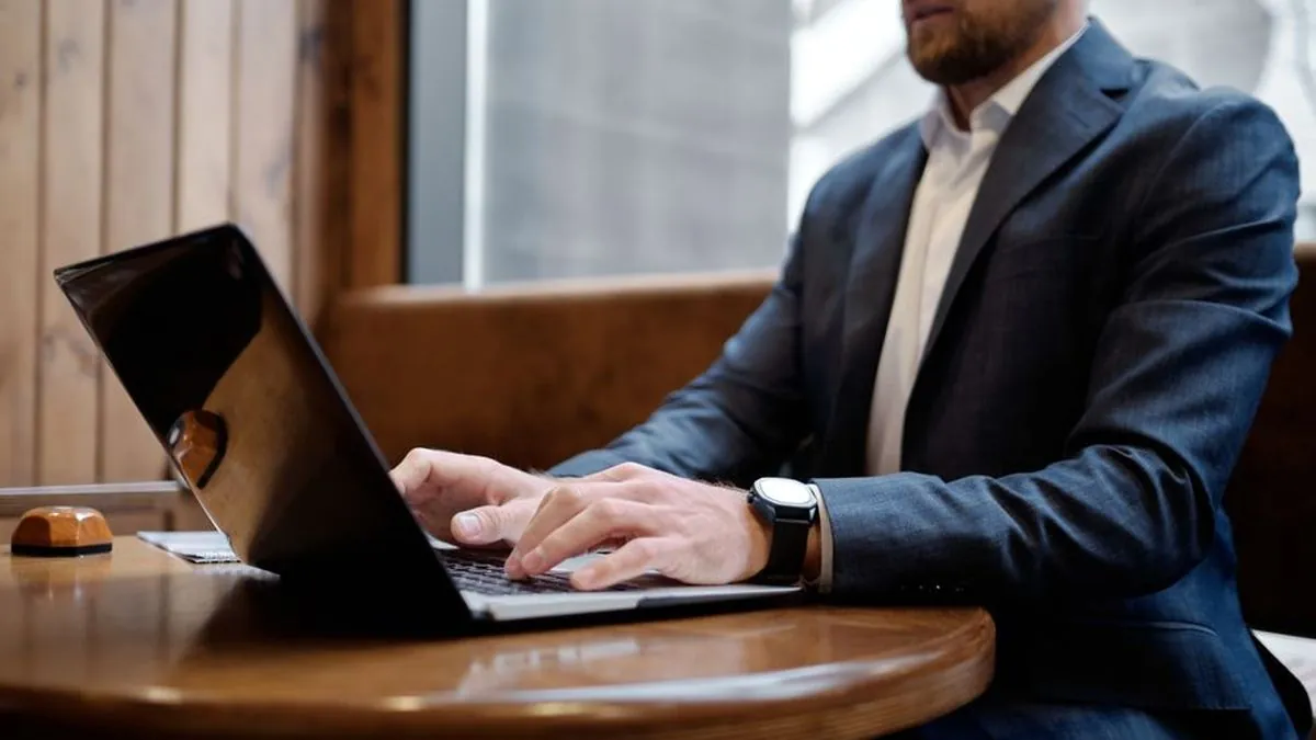Businessman in a suit typing on a laptop at a wooden table