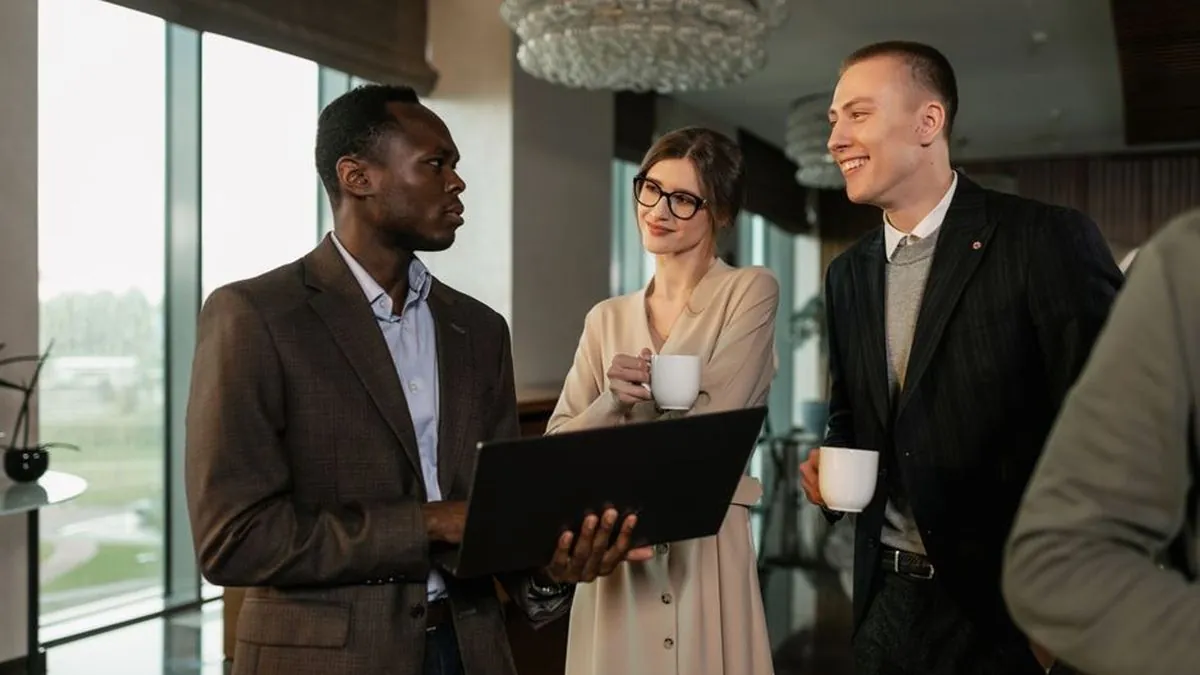 Business professionals chatting with a laptop and coffee in a bright office