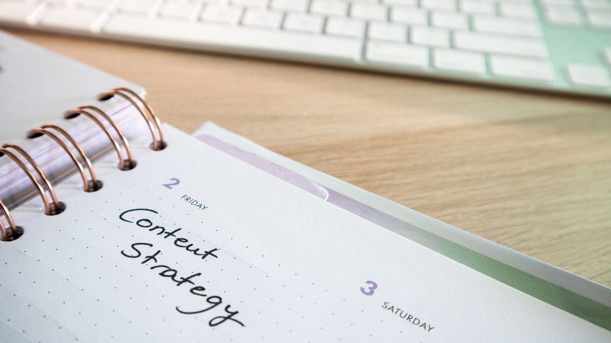 Planner open to a content strategy page beside a keyboard on a wooden desk