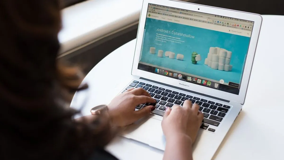 Person typing on a laptop at a white desk with a website open on screen