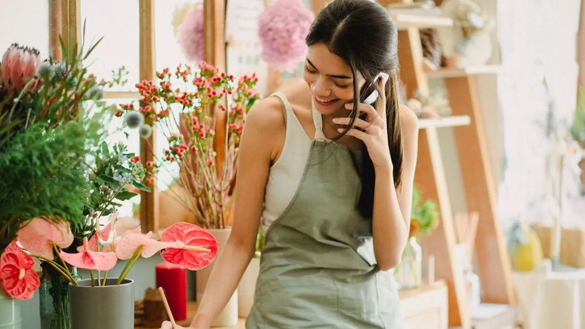 Florist smiling while talking on a phone and noting an order in a flower shop