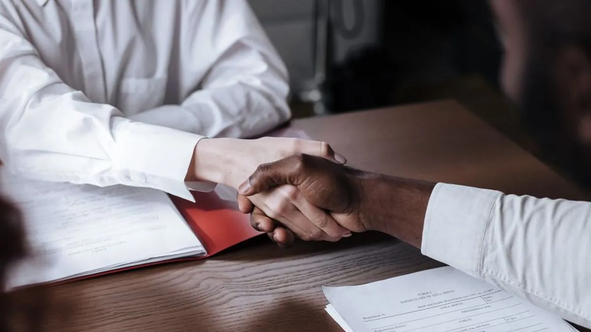 Two people shaking hands over contract papers on a wooden desk