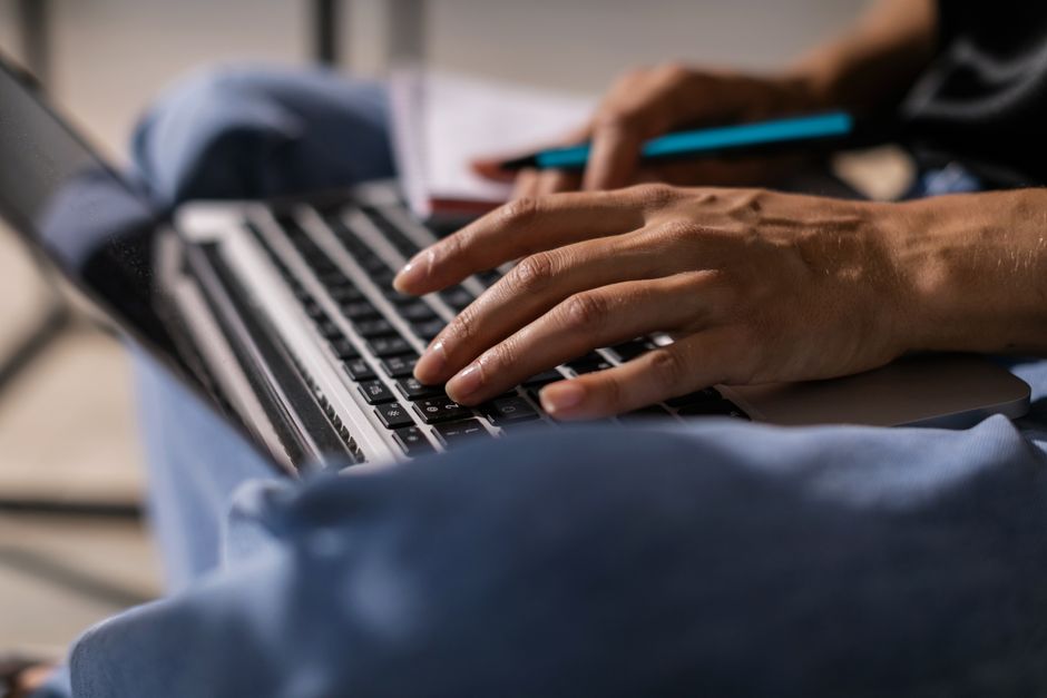 Content writer typing an article on a laptop with a notebook nearby
