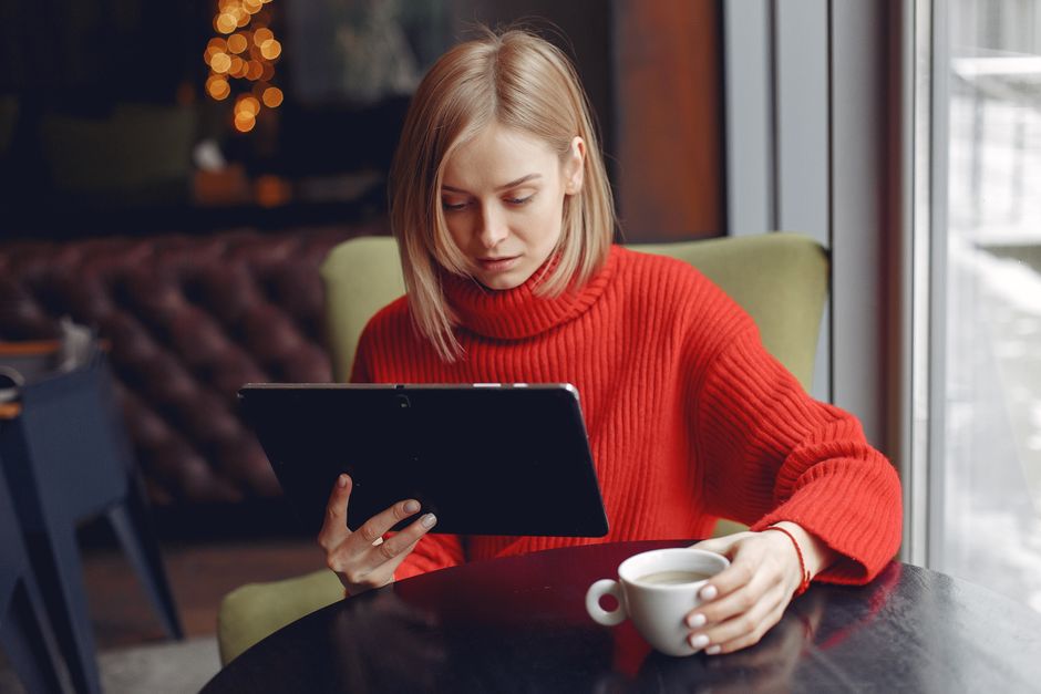 Woman in a red sweater reading an email on a tablet in a cafe
