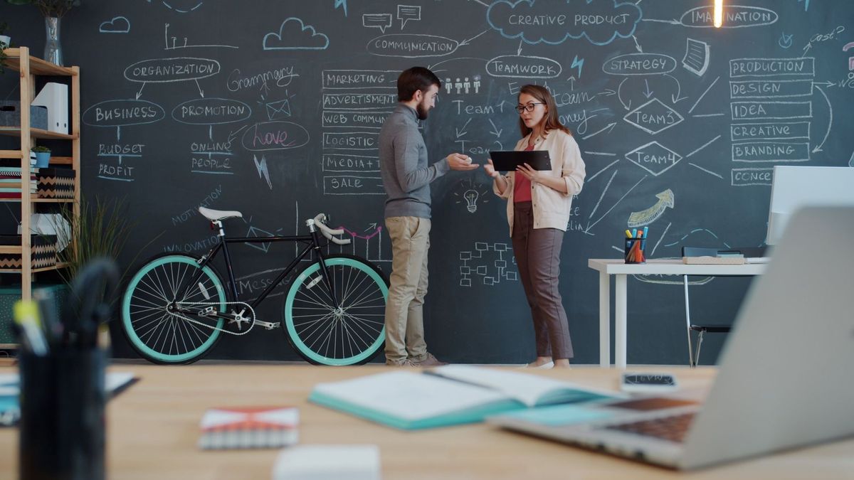 Two colleagues planning a website project at a chalkboard wall in a bright office