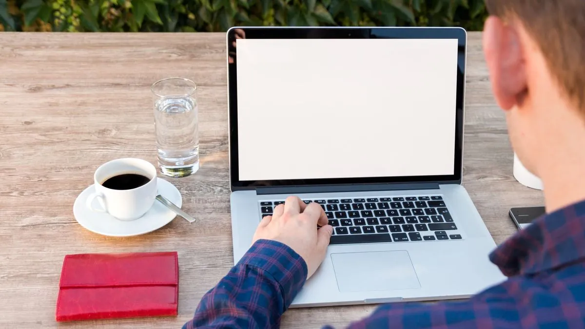 Person typing on a laptop at a wooden desk beside a cup of coffee