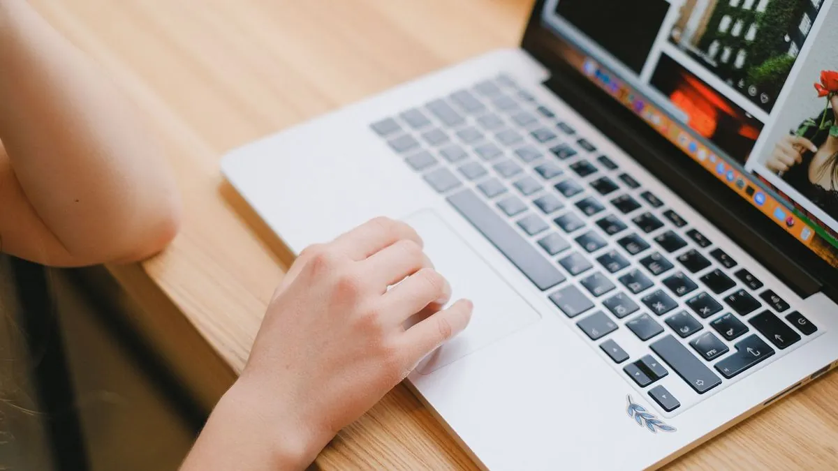 Hand resting on a laptop trackpad while searching on a wooden desk