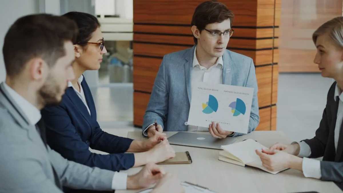 Colleagues at a meeting table reviewing printed charts with a laptop