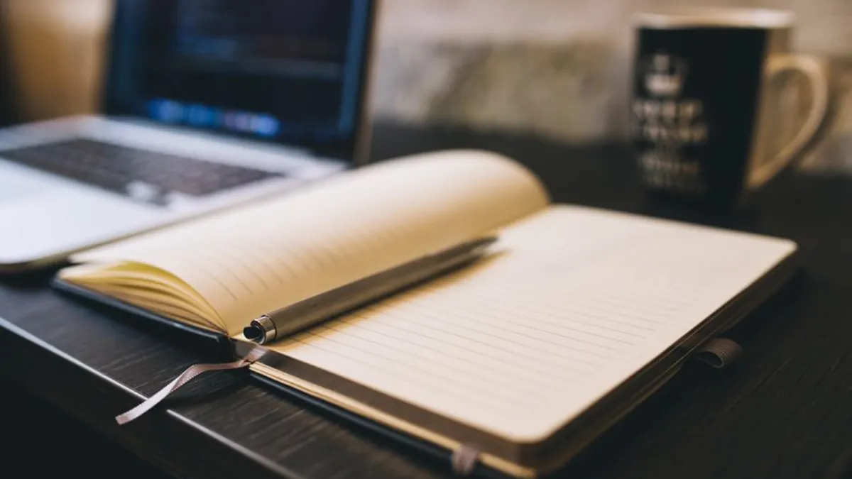 Open notebook with a pen beside a laptop on a dark desk for writing down brand decisions