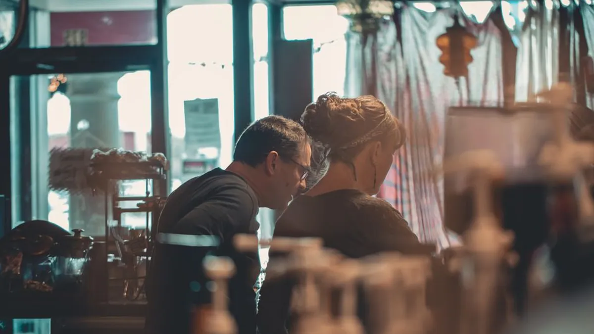 Two people talking closely at a cafe counter during a customer conversation