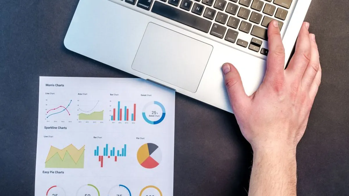 Laptop on a desk beside a printed sheet of marketing analytics charts