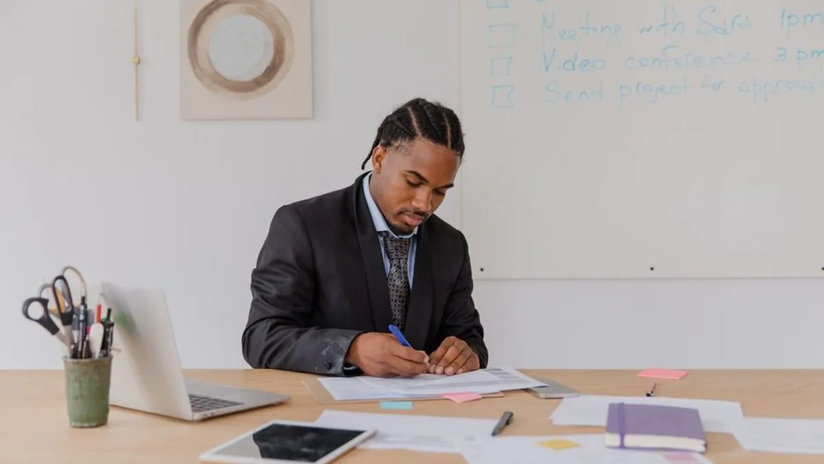 Business owner writing a plan at a desk in front of a whiteboard task list