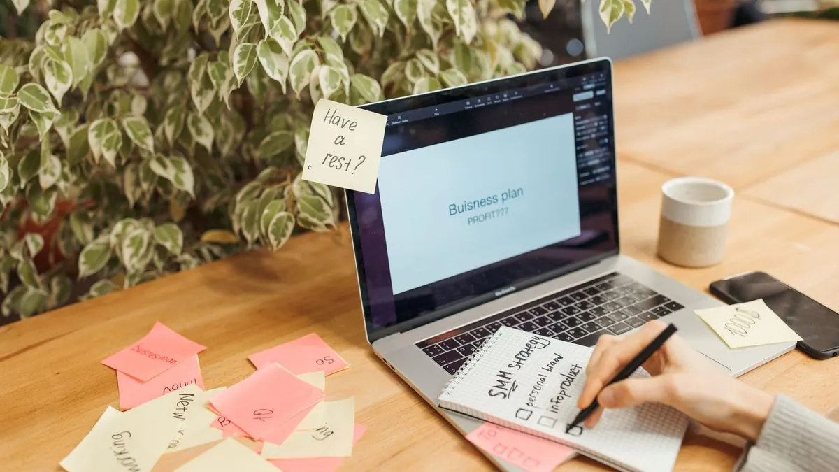 Laptop showing a business plan slide beside sticky notes and a notebook with a social media plan