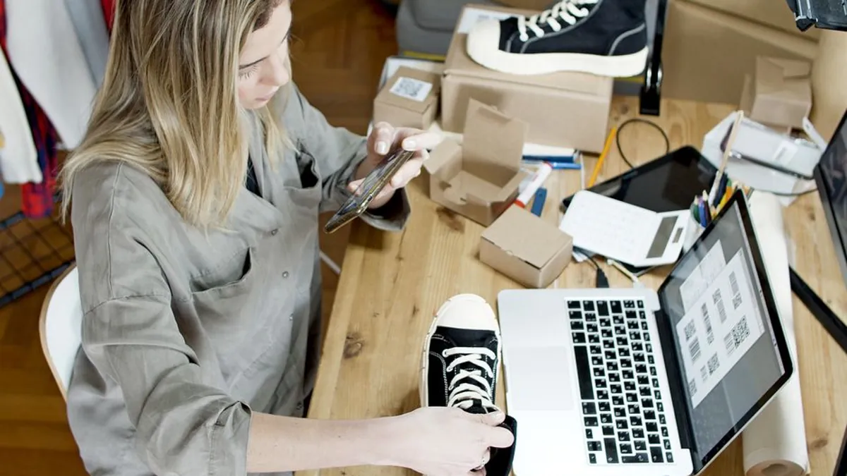 Online store owner packing sneakers beside a laptop and parcels at a wooden desk