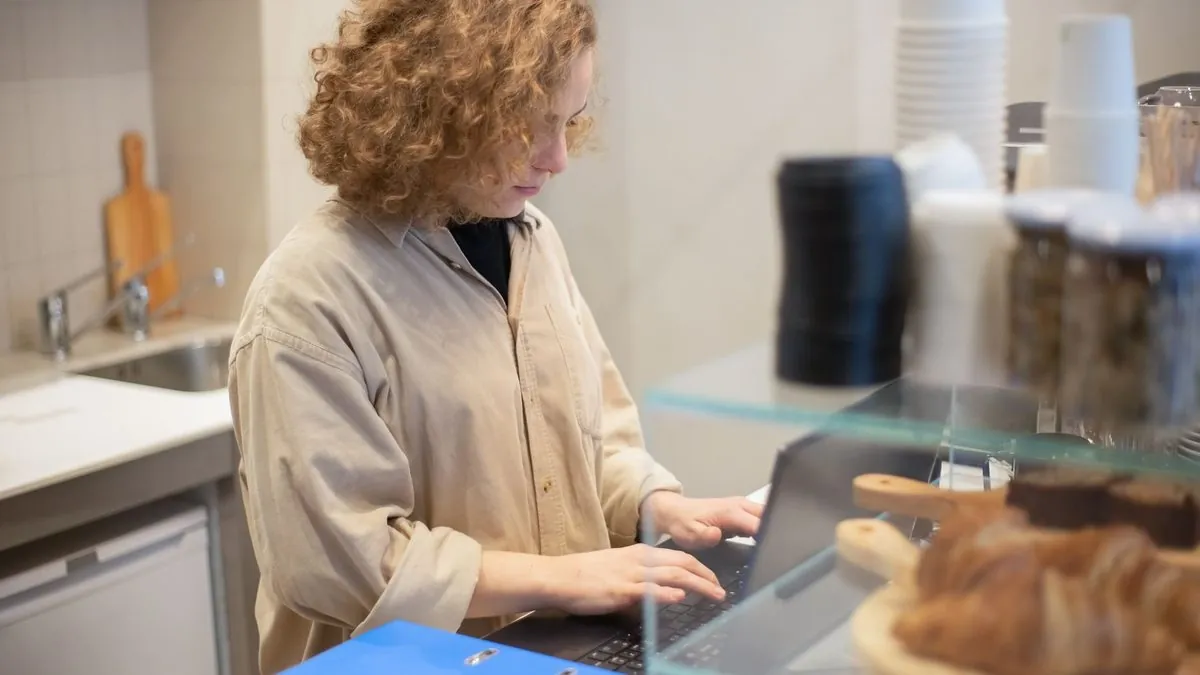 Small business owner typing on a laptop behind a cafe counter with pastries in the foreground
