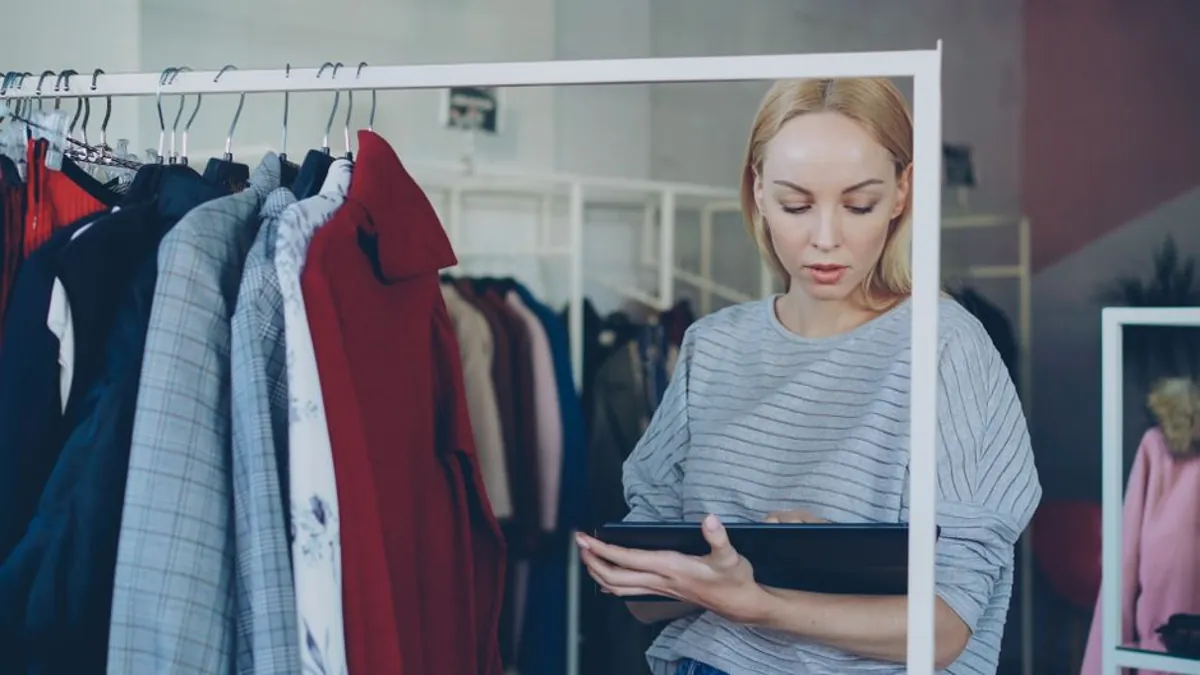 Boutique owner checking a tablet beside a rack of clothes in her shop