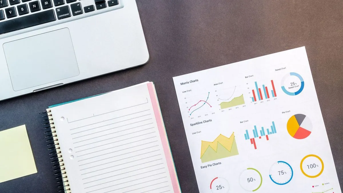 Laptop, notebook and printed charts on a desk for planning a marketing strategy