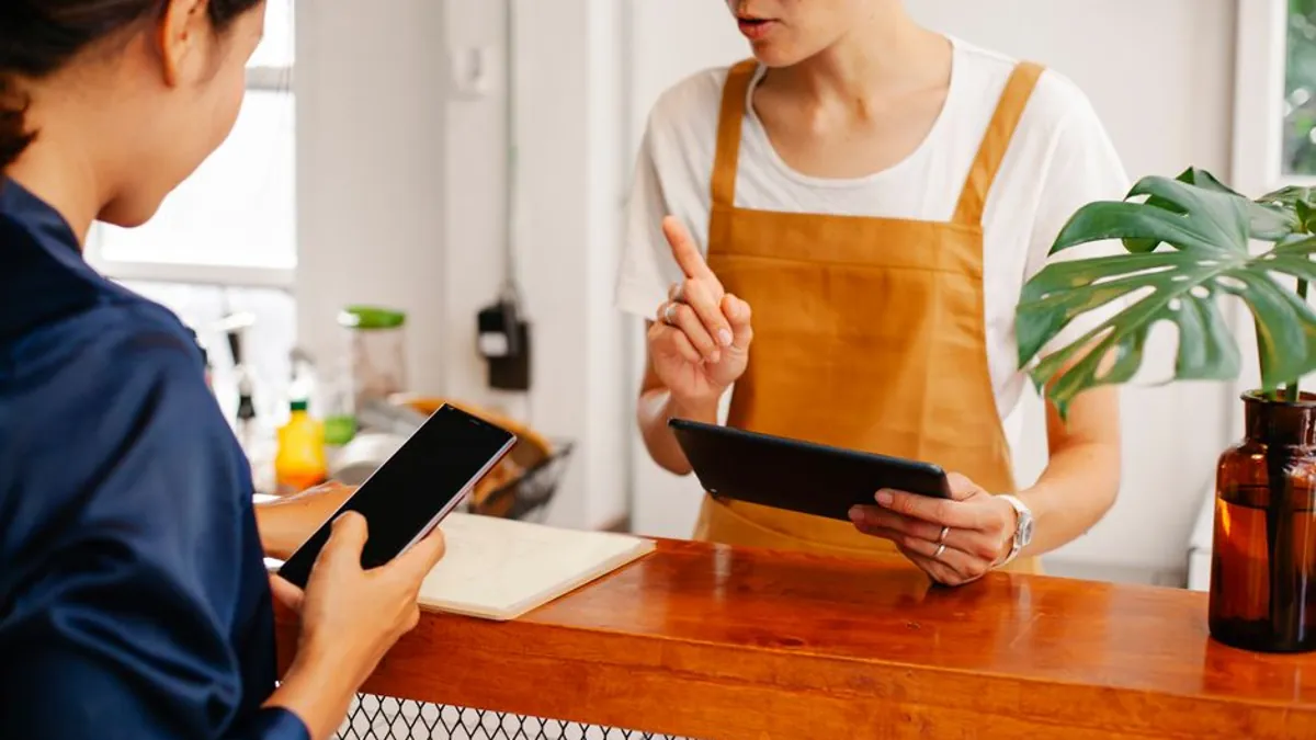 Shop owner showing a tablet to a customer holding a smartphone at a counter
