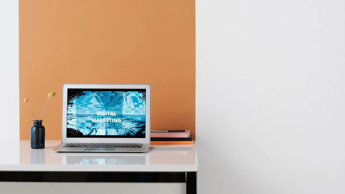 Laptop showing a digital marketing screen on a clean white desk against an orange wall