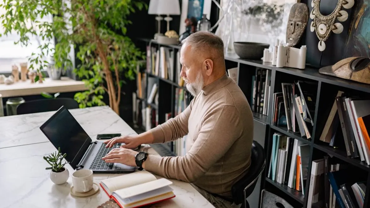 Business owner working on a laptop at a desk with a notebook and cup beside it