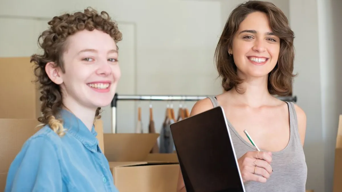Two smiling shop owners with a laptop and stock boxes planning their online marketing