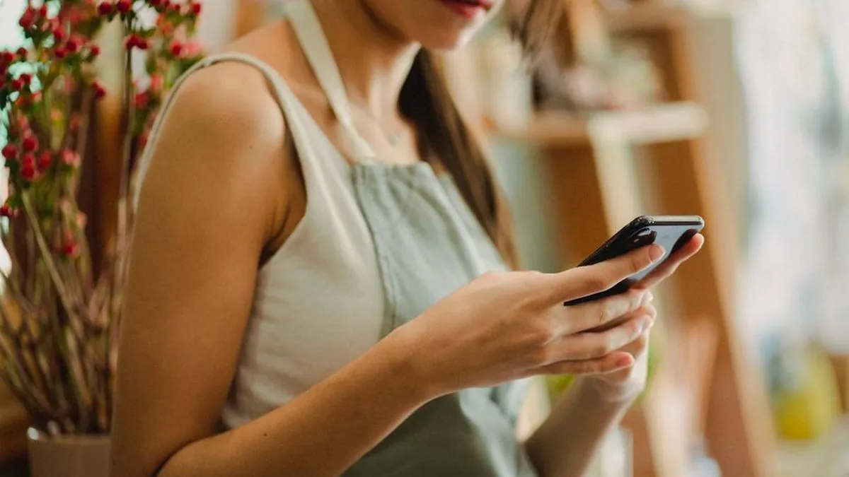 Woman checking a smartphone beside a shelf while reading a social media post