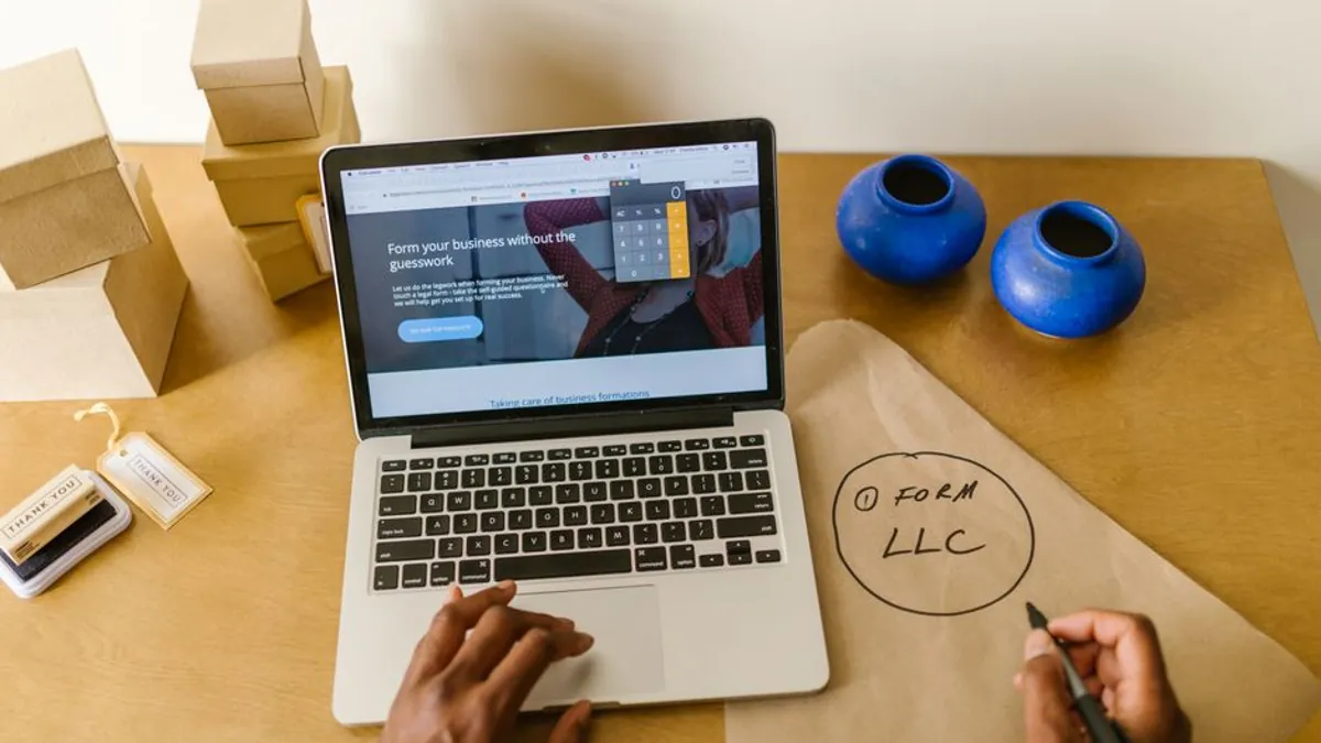 Business owner at a laptop beside small shipping boxes sketching a first step on brown paper