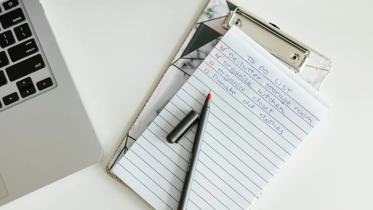 Handwritten to-do list on a clipboard with a pen next to a laptop