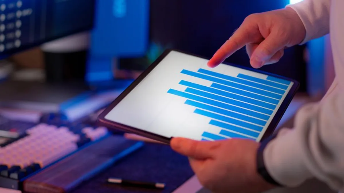 Person pointing at a bar chart on a tablet beside a keyboard