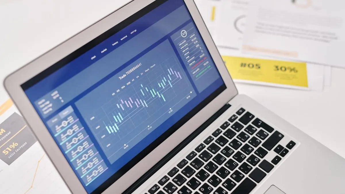 Laptop showing a performance chart beside printed reports