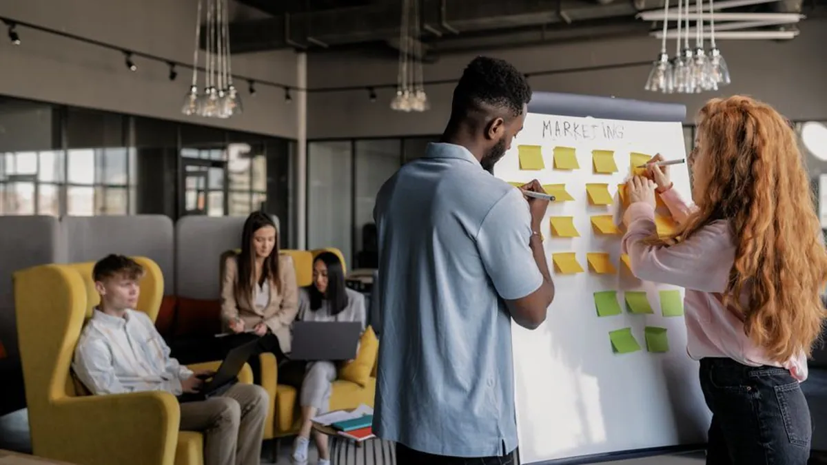 Two colleagues arranging sticky notes on a whiteboard headed marketing