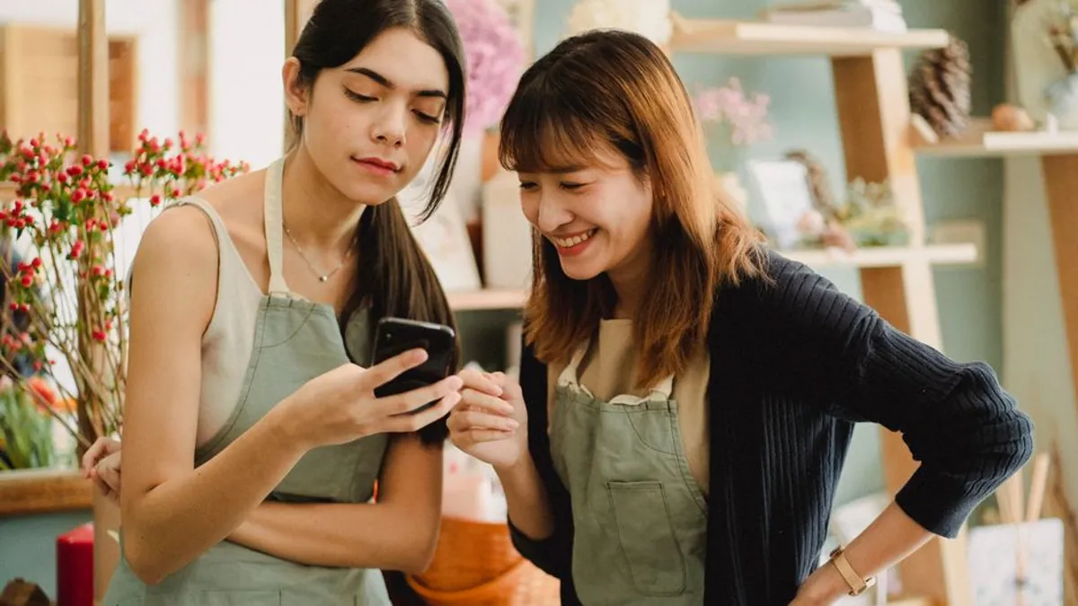 Florists in aprons looking at a mobile phone together in a flower shop