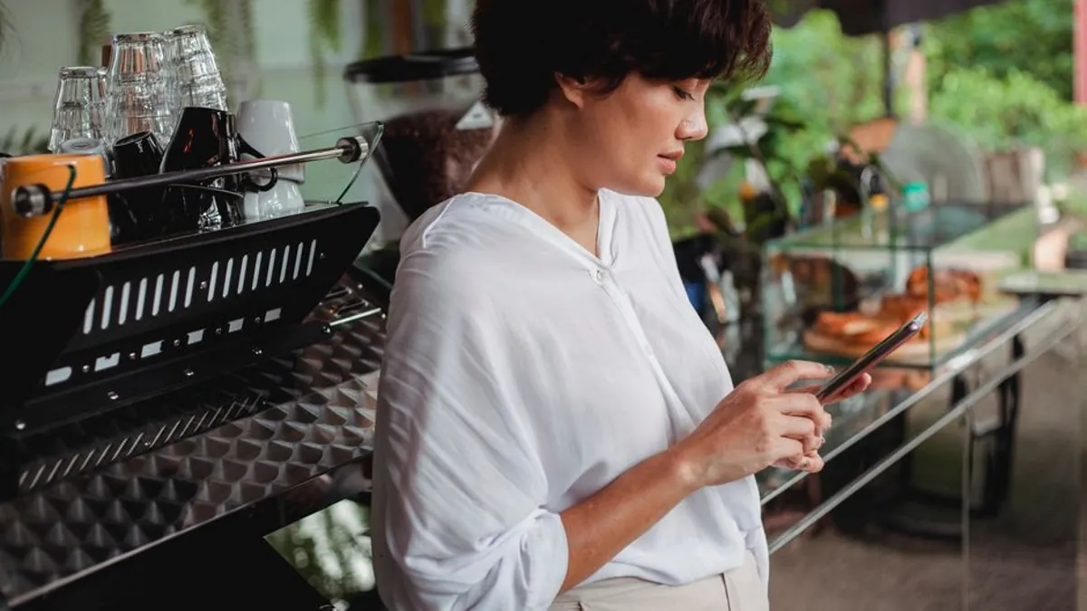 Woman checking her phone beside a cafe counter while planning a post