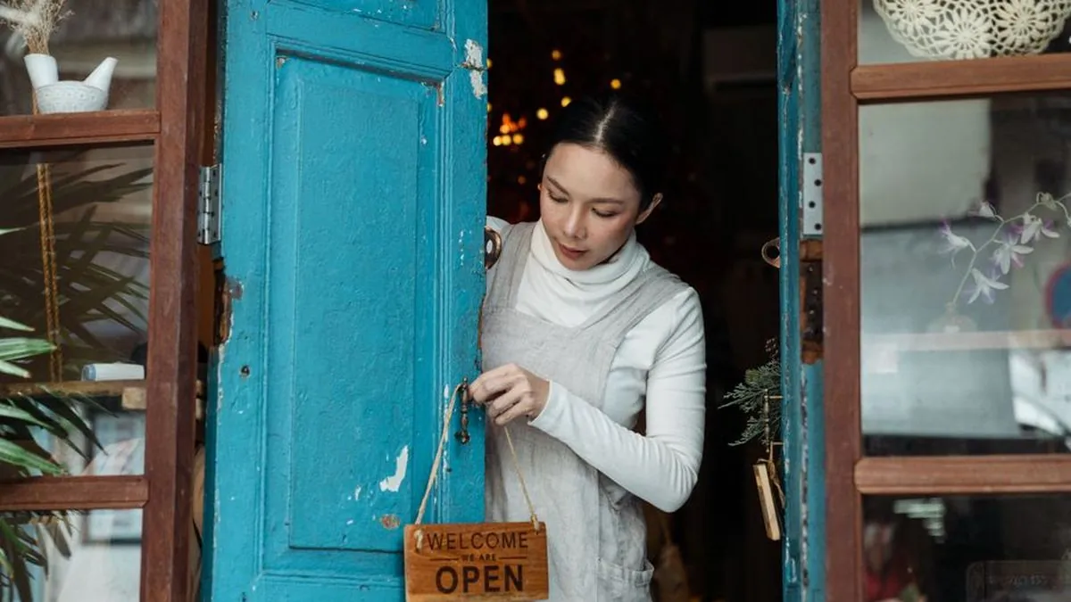 Shop owner turning an open sign on the door of a small storefront